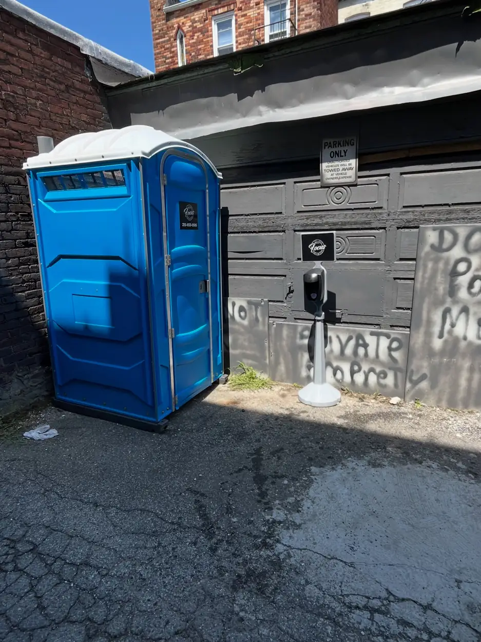 Standard porta potty placed out of sight behind a building